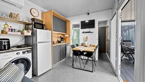Une cuisine compacte équipée d’un réfrigérateur, d’un four à micro-ondes et d’un lave-linge. Elle comprend un coin repas avec une table et des chaises, ainsi qu’un téléviseur fixé au mur.
