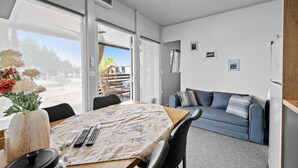 Une pièce moderne comprenant une table à manger, des chaises, un canapé et une vue sur l’extérieur, visible à travers la porte vitrée.