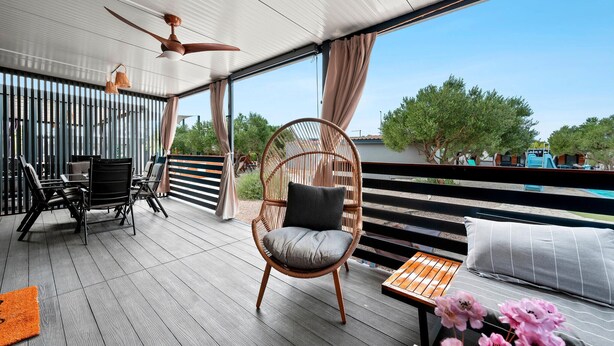 Un espace extérieur abrité, doté d'un ventilateur de plafond, de chaises en osier, d'une table et offrant une vue sur les arbres et une piscine.