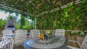 Eine Terrasse im Freien mit einem runden Tisch, weißen Stühlen und einer Obstschale.