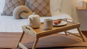 A neatly made bed with patterned pillows, a bedside table with a tray holding a teapot, a cup, and a plate with a fruit. - Wings Apartment II – With Balcony in Santa Cruz (Santa Cruz)