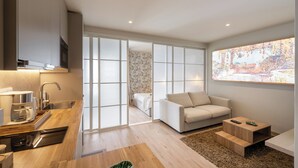 A modern living space with a kitchen, a sofa, a coffee table, and a large window with a view.