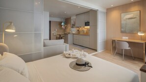 A modern hotel room with a large bed, a desk, and a view into the kitchen.