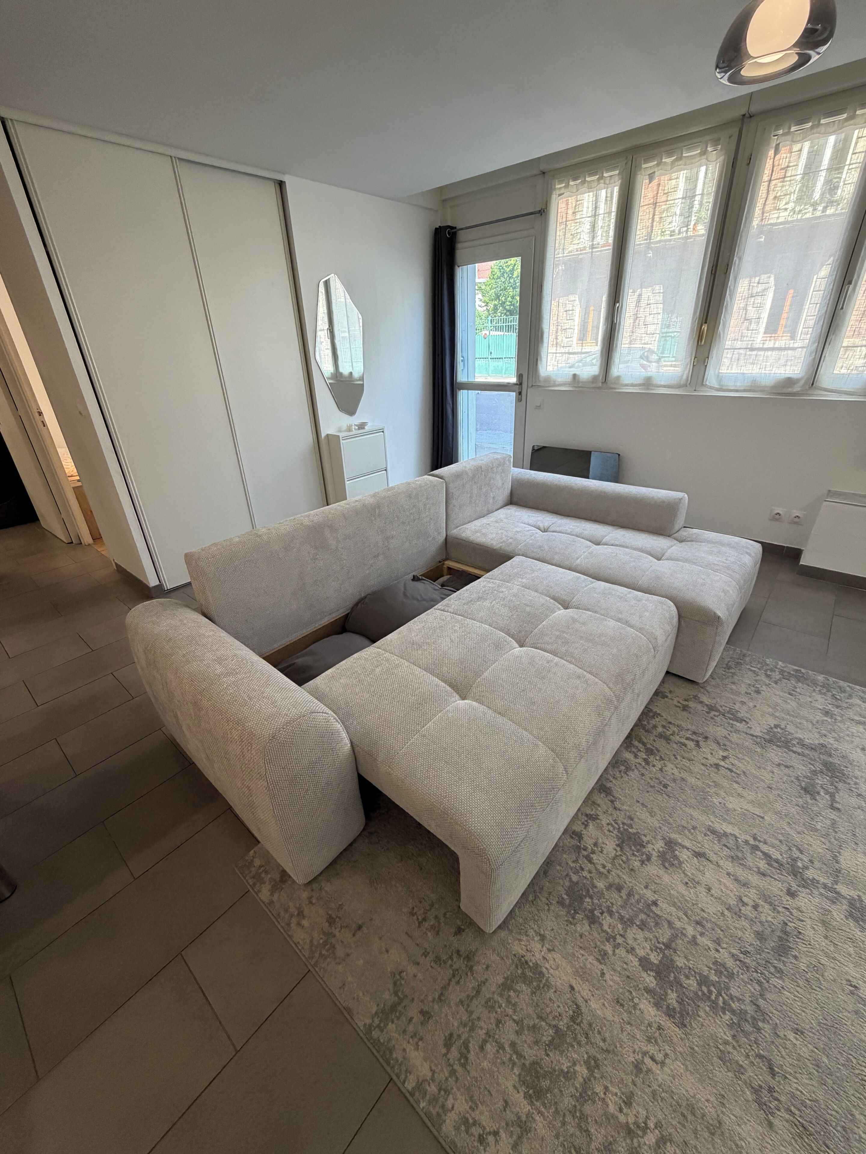 A modern living room with a sectional sofa, a flat-screen TV, and a large window with curtains.