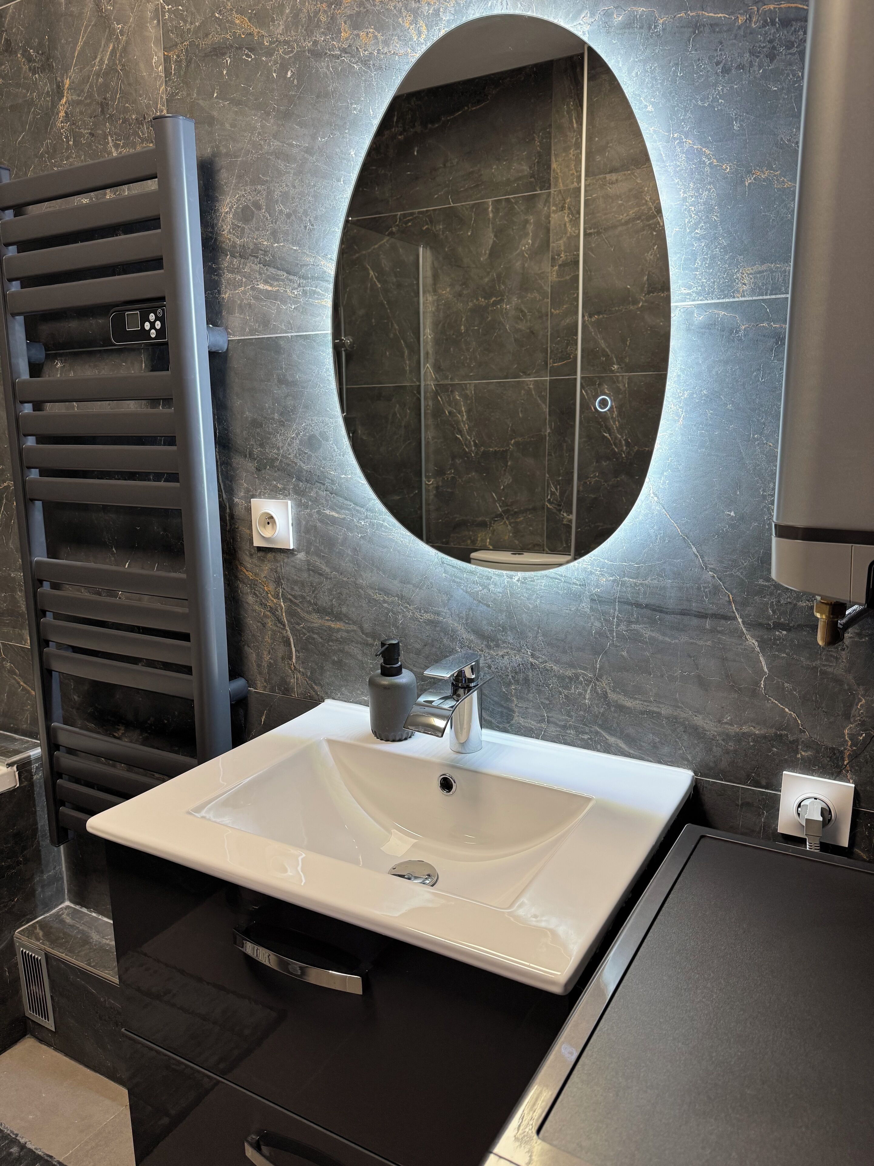 Une salle de bain avec un lavabo blanc, un miroir rond, un porte-serviettes et un espace douche.