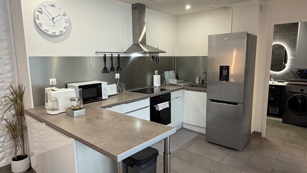 Une cuisine moderne avec un îlot central, des appareils en acier inoxydable et une horloge au mur.
