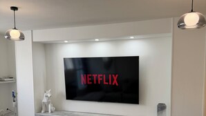 Un salon moderne doté d’un téléviseur à écran plat fixé au mur, d’une table basse en verre et d’un design minimaliste.