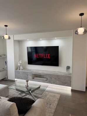 Ein modernes Wohnzimmer mit Flachbildfernseher an der Wand, einem Glastisch und einem minimalistischen Design.