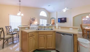 A kitchen with wooden cabinets, a dishwasher, and a dining area with chairs and a table. - Highgate Palace-near Disney World. 20min Drive (Davenport)
