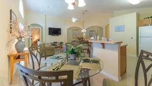 Une cuisine moderne dotée d’un îlot central, d’un coin repas avec une table ronde et des chaises, et d’un espace de détente avec des canapés et un téléviseur à écran plat.
