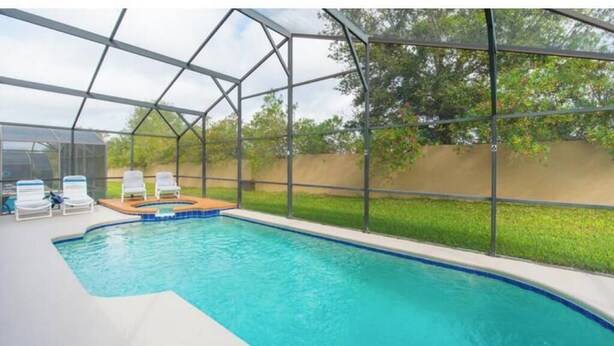 Une piscine dotée d’une enceinte en verre, entourée de chaises longues et d’une terrasse en bois.
