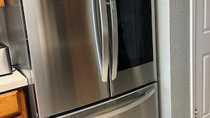 A stainless steel refrigerator with a freezer compartment, located in a kitchen with wooden cabinets and a tiled floor.