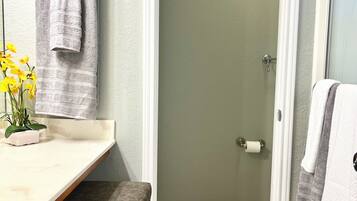 Un bagno con un lavabo bianco, una panca, un portascopevoli con asciugamani, un porta carta igienica e una pianta in vaso.