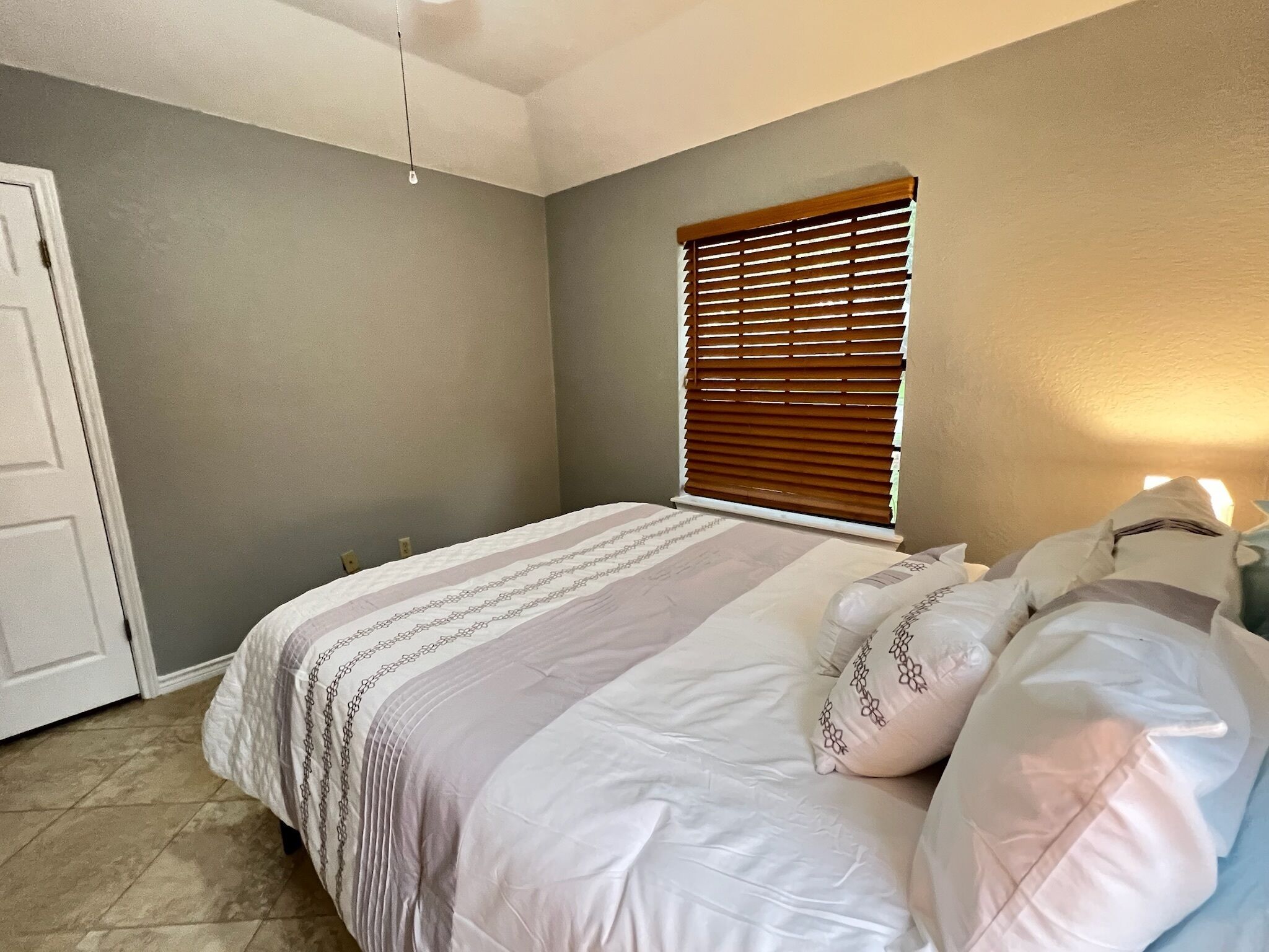 A bedroom with a bed, a window with blinds, a door, and a light fixture.