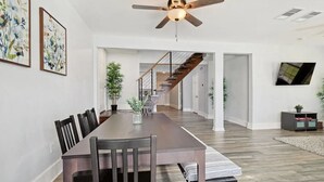 A spacious dining area with a long wooden table, black chairs, and a ceiling fan.