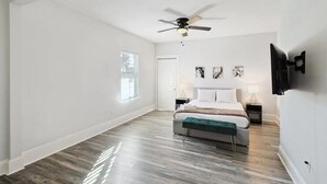 A spacious bedroom with a large bed, a ceiling fan, a mounted TV, and artwork on the wall.