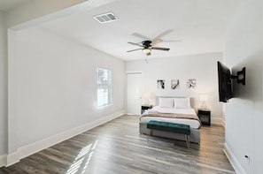 Un dormitorio amplio con una cama grande, un ventilador de techo, un televisor montado y obras de arte en la pared.