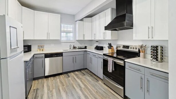 A modern kitchen with white cabinets, stainless steel appliances, and a wood-patterned floor.