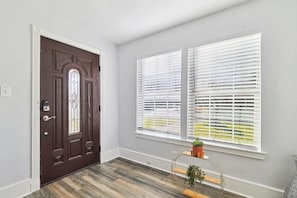 Una habitación con una puerta marrón oscuro, detalles blancos y una ventana con persianas blancas.