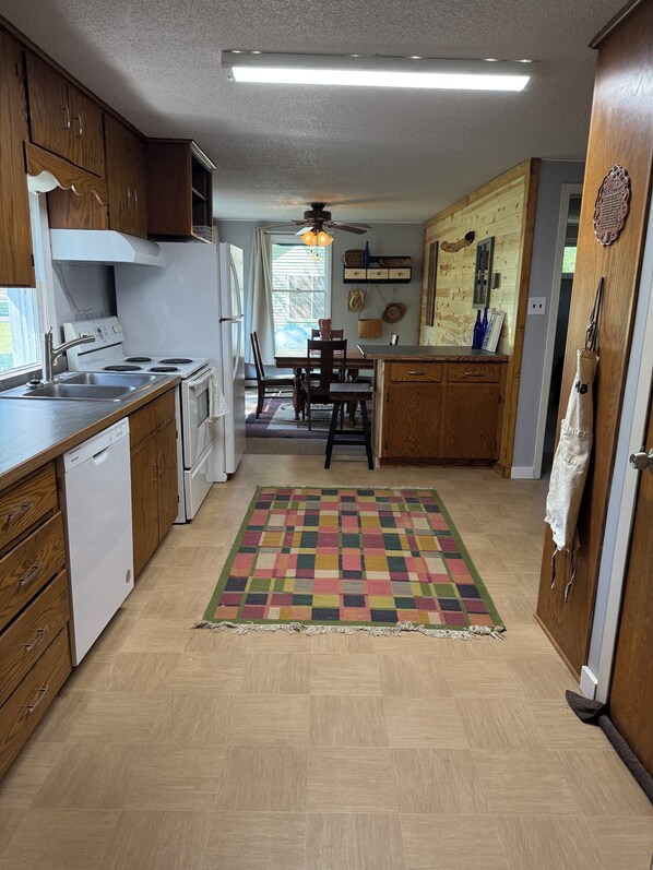 Une cuisine de taille réduite, avec des meubles de rangement en bois, un fourneau blanc et un tapis aux couleurs vives.