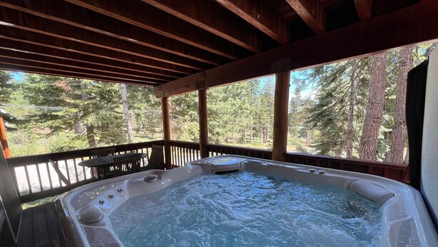 Un bain à remous installé sur une terrasse en bois, avec vue sur une forêt.