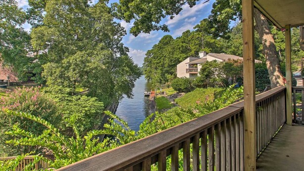 A wooden deck overlooking a river, surrounded by lush greenery and a residential building.