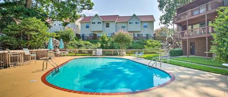 A swimming pool with a wooden deck and lounge chairs, surrounded by a fence and trees.