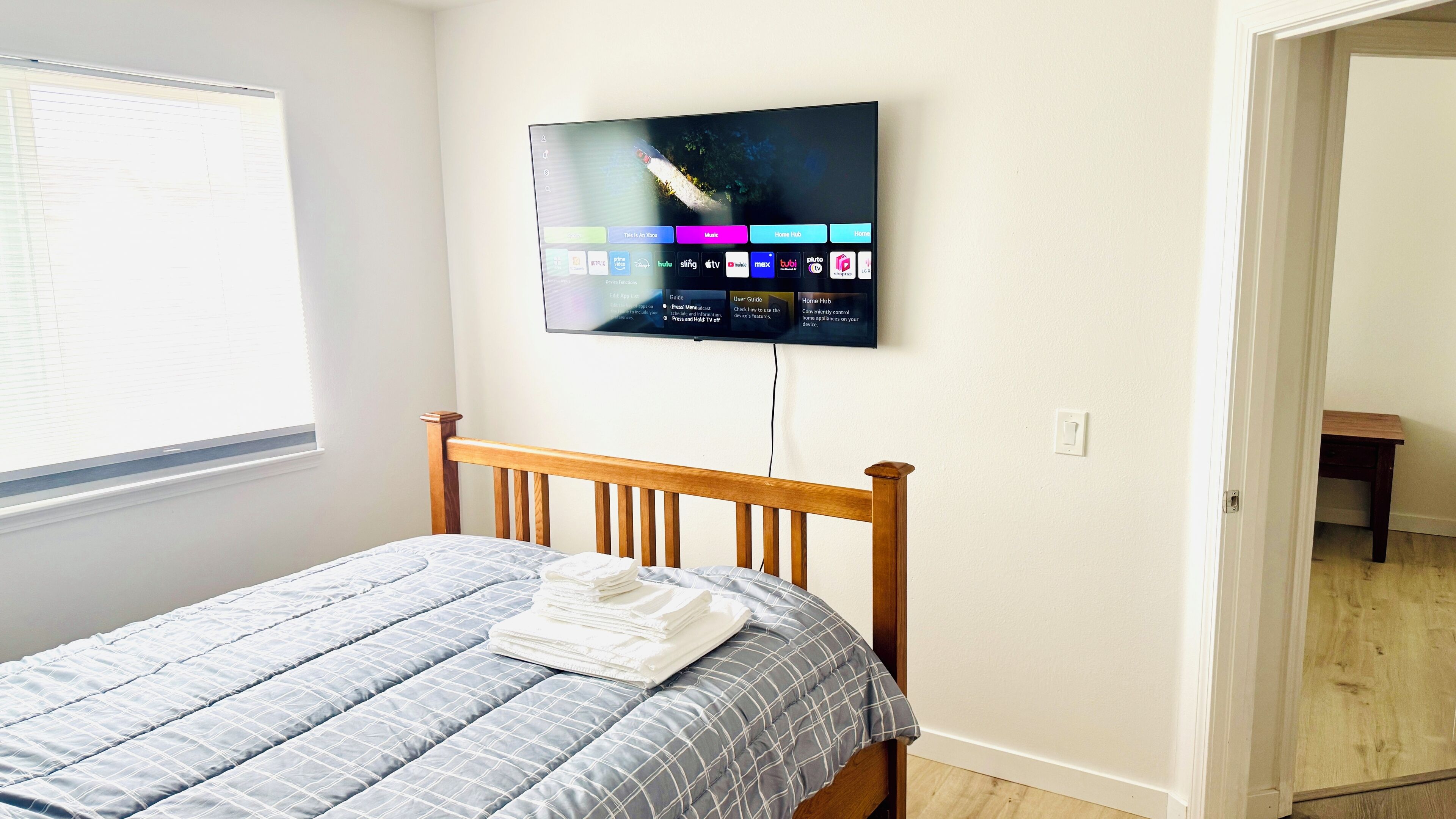 Ein Schlafzimmer mit einem Bett, einem an der Wand befestigten Fernseher und einem Fenster.