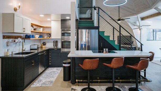 Une cuisine moderne avec des meubles de couleur sombre, des appareils en acier inoxydable et un coin bar équipé de tabourets.