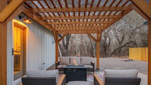 Une terrasse extérieure agrémentée d’une pergola en bois, d’un foyer et de meubles en osier.