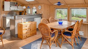 Een knus houten interieur met een eethoek, een keuken met een inbouwfornuis en grote ramen met uitzicht op de omgeving.