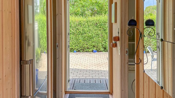 Een houten deur die uitkomt op een geplaveid gebied met een bankje en een kleine tuin.