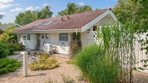 Een gelijkvloers huis met een rode pannendak, een klein terras en een tuin met verschillende planten.