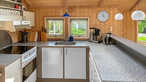 Een keuken met granieten aanrecht, een inbouwoven, een spoelbak en een koffiezetapparaat. Er zijn houten kastjes, een klok en een raam met uitzicht op groen.