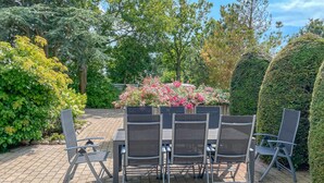 Een terras buiten met een tafel en stoelen, omringd door weelderige begroeiing en bloeiende planten.