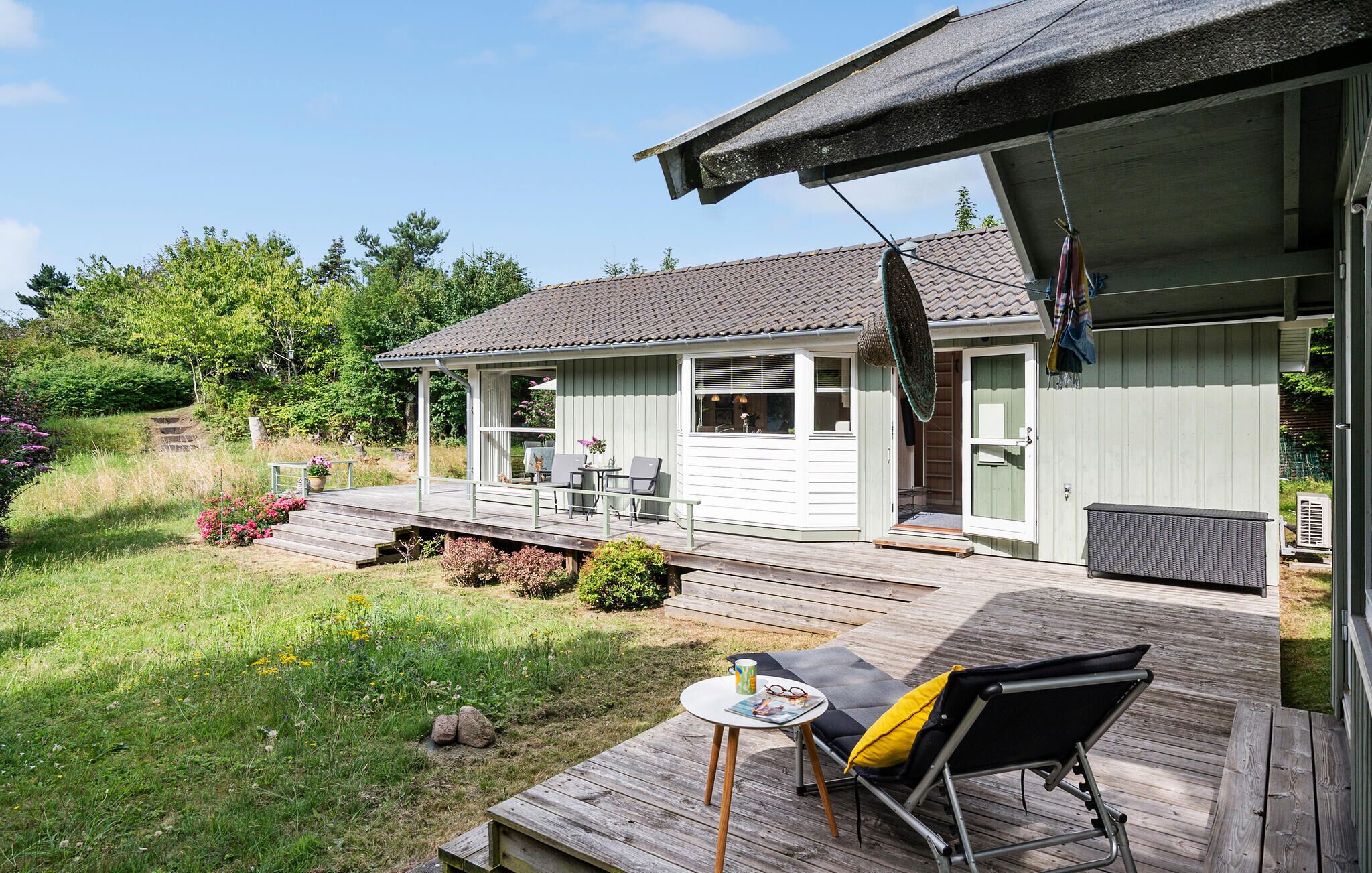 A wooden deck with a table and chairs, a covered outdoor area, and a house with a tiled roof.