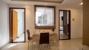 A dining area with a table and chairs, a window with blinds, and a door leading to another room. - Apto c Conforto Tecnologia a 10 min do Aeroporto (Nucleo Bandeirante)