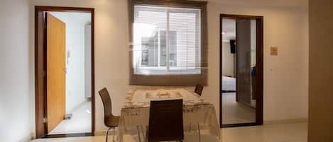 A dining area with a table and chairs, a window with blinds, and a door leading to another room.