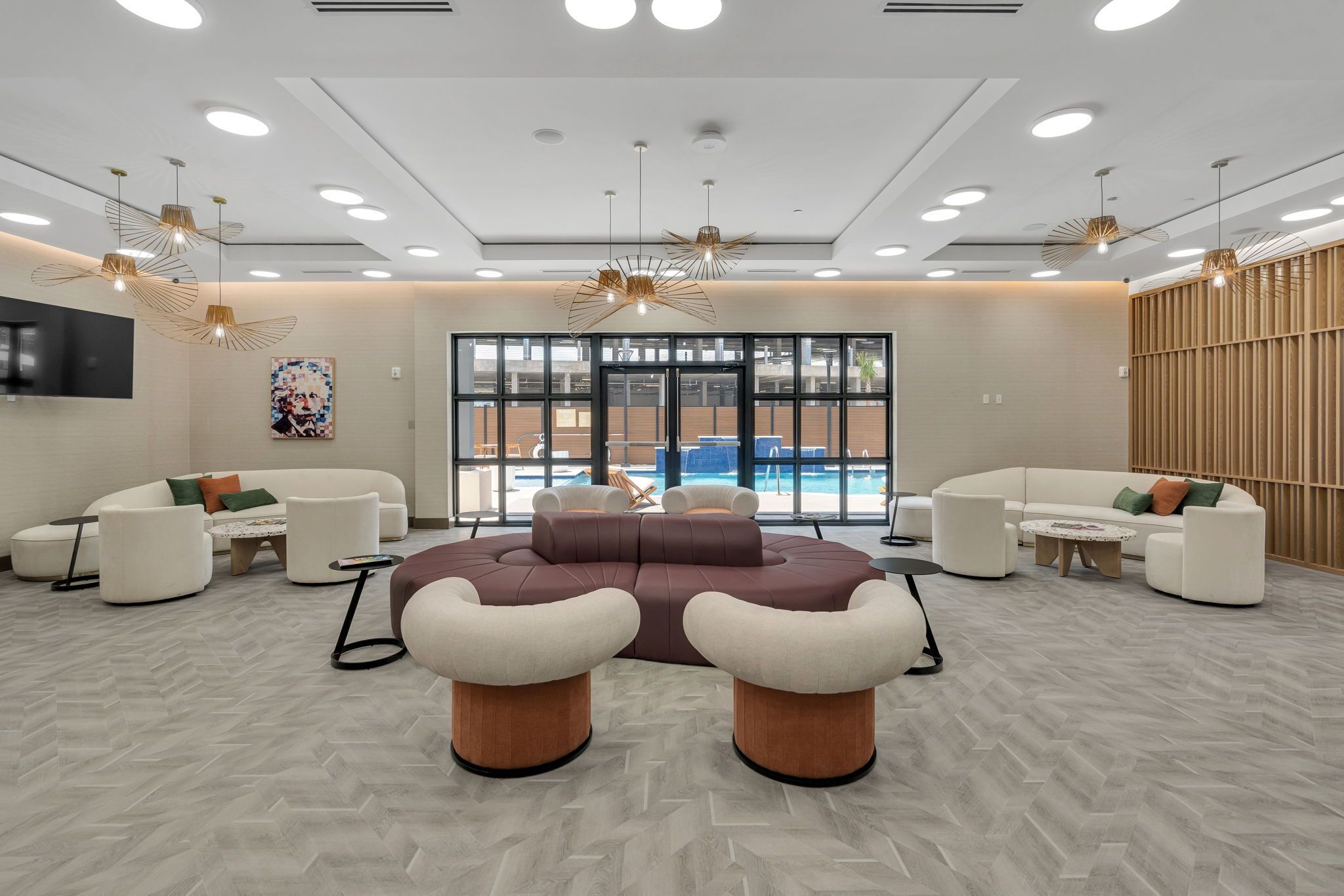 Un hall d’entrée moderne avec un grand canapé d’angle, des poufs ronds et une vue sur la piscine.
