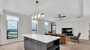 A modern kitchen with a large island, a dining area with a sofa and chairs, a TV, and a ceiling fan. - Latitude Apartments (Metairie)