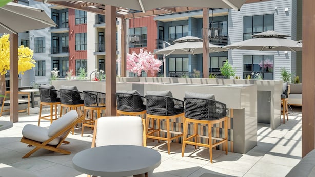 A rooftop bar with outdoor seating, including chairs and a sofa, and a bar counter. - Latitude Apartments (Metairie)