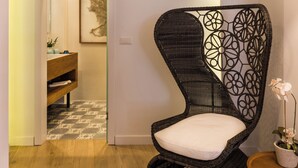 A wicker chair with a geometric pattern, a wooden floor, and a doorway leading to a bathroom with a sink and mirror. - Upscale 2-bedroom villa in the Venetian Harbour (Chania)