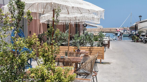 A seaside café with outdoor seating, a view of the marina, and a clear blue sky. - Upscale 2-bedroom villa in the Venetian Harbour (Chania)