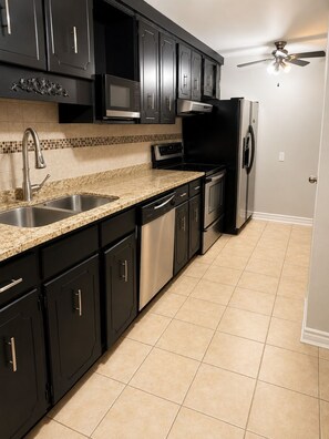 A kitchen with black cabinets, stainless steel appliances, a granite countertop, and a tiled floor.