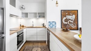 Een moderne keuken met witte kasten, een houten aanrecht en een decoratief abstract schilderij.