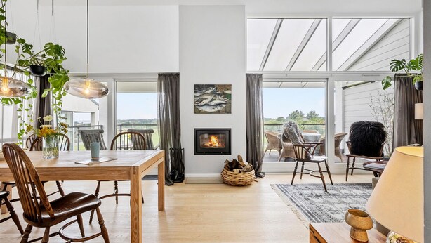 Een ruime eethoek met een houten tafel en stoelen, een open haard en grote ramen met uitzicht op de omgeving.