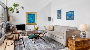 Een moderne woonkamer met een bank, een houten salontafel, een televisie en kunst aan de muur.