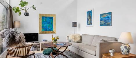 A modern living room with a sofa, a wooden coffee table, a TV, and artwork on the wall.