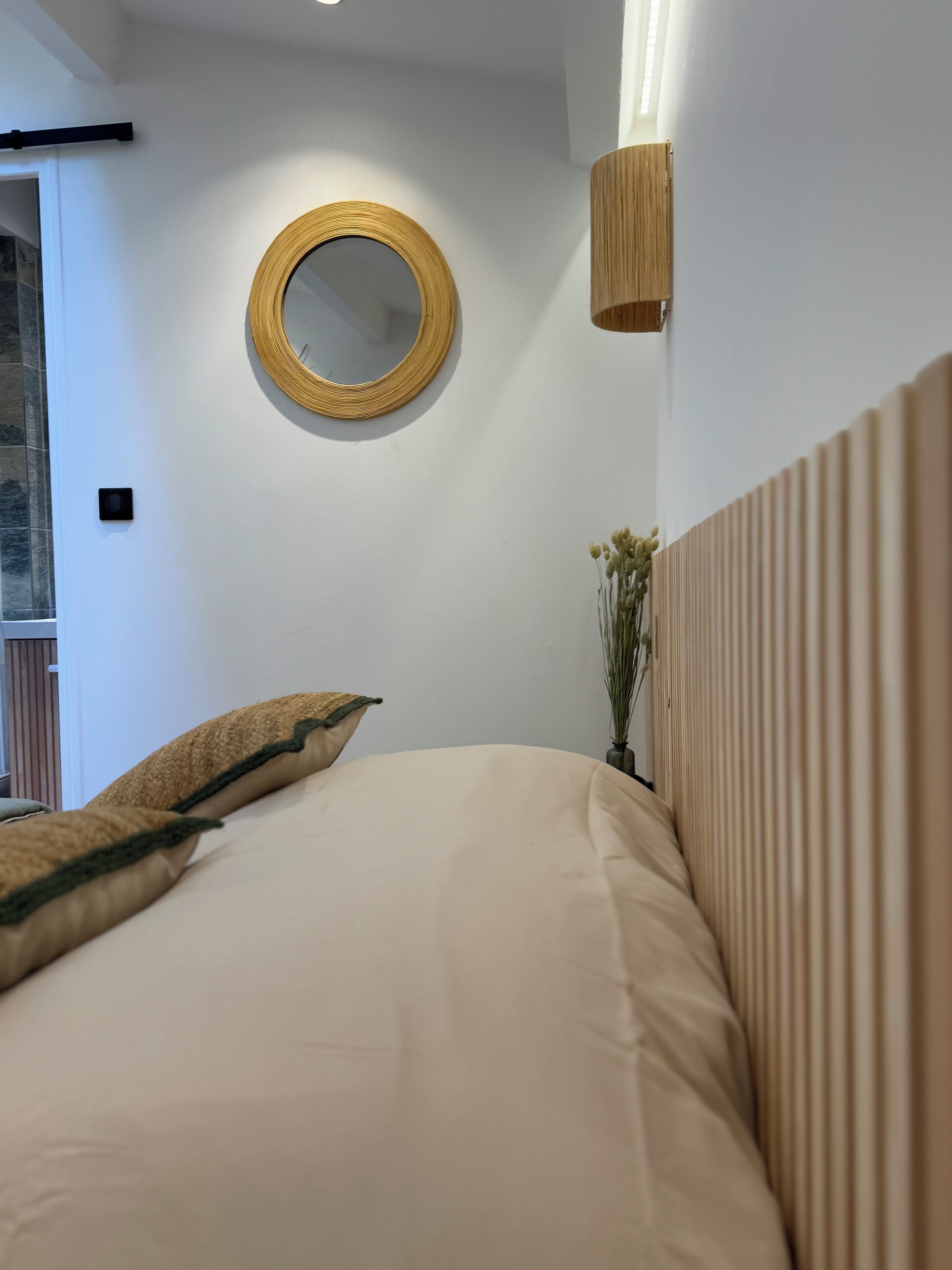 Ein Schlafzimmer mit einem Bett, einem runden Spiegel, einer Wandleuchte und einem Fenster mit Ausblick.