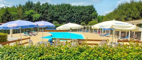 A pool area with lounge chairs and umbrellas, surrounded by greenery.